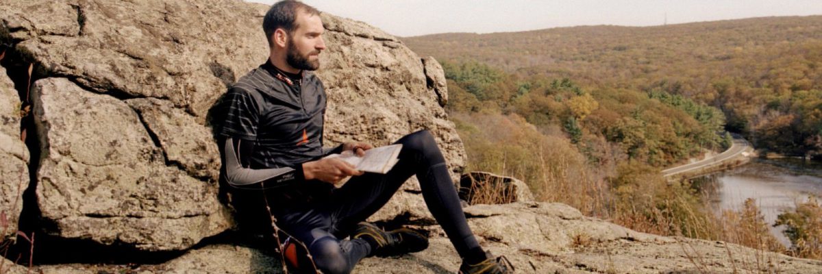 Thierry GUEORGIOU lit une carte assis sur un rocher